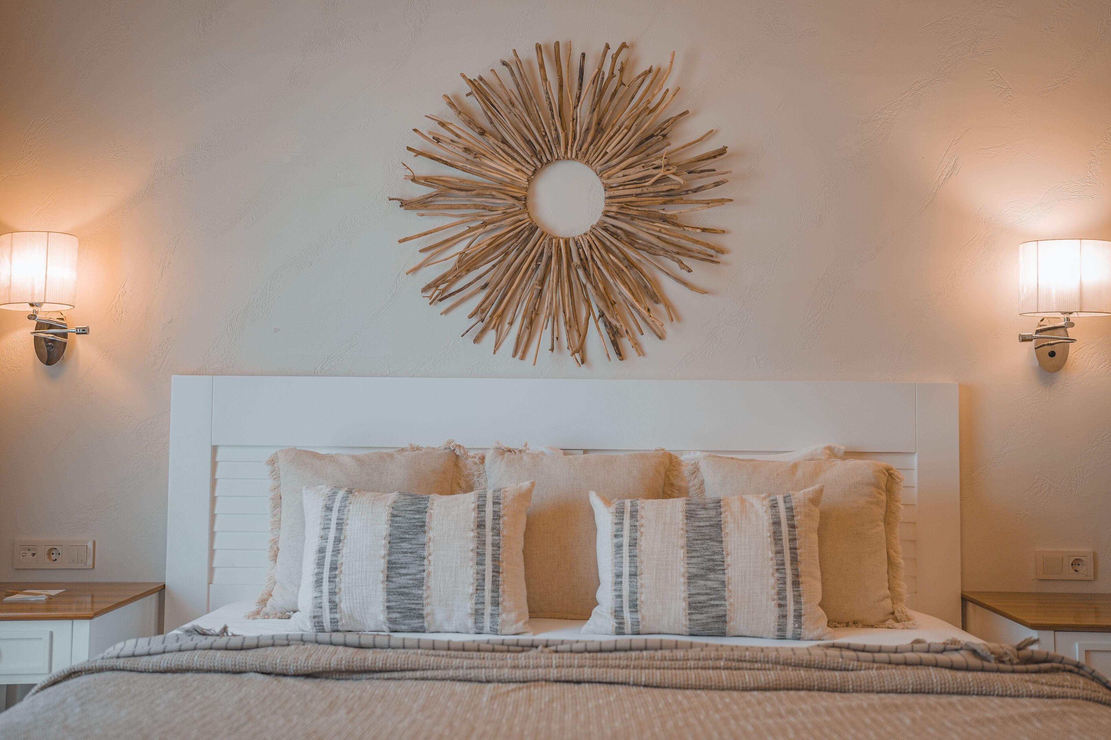 A neatly made bed with a white headboard, flanked by two bedside tables with lamps, and a sunburst wall decoration above.
