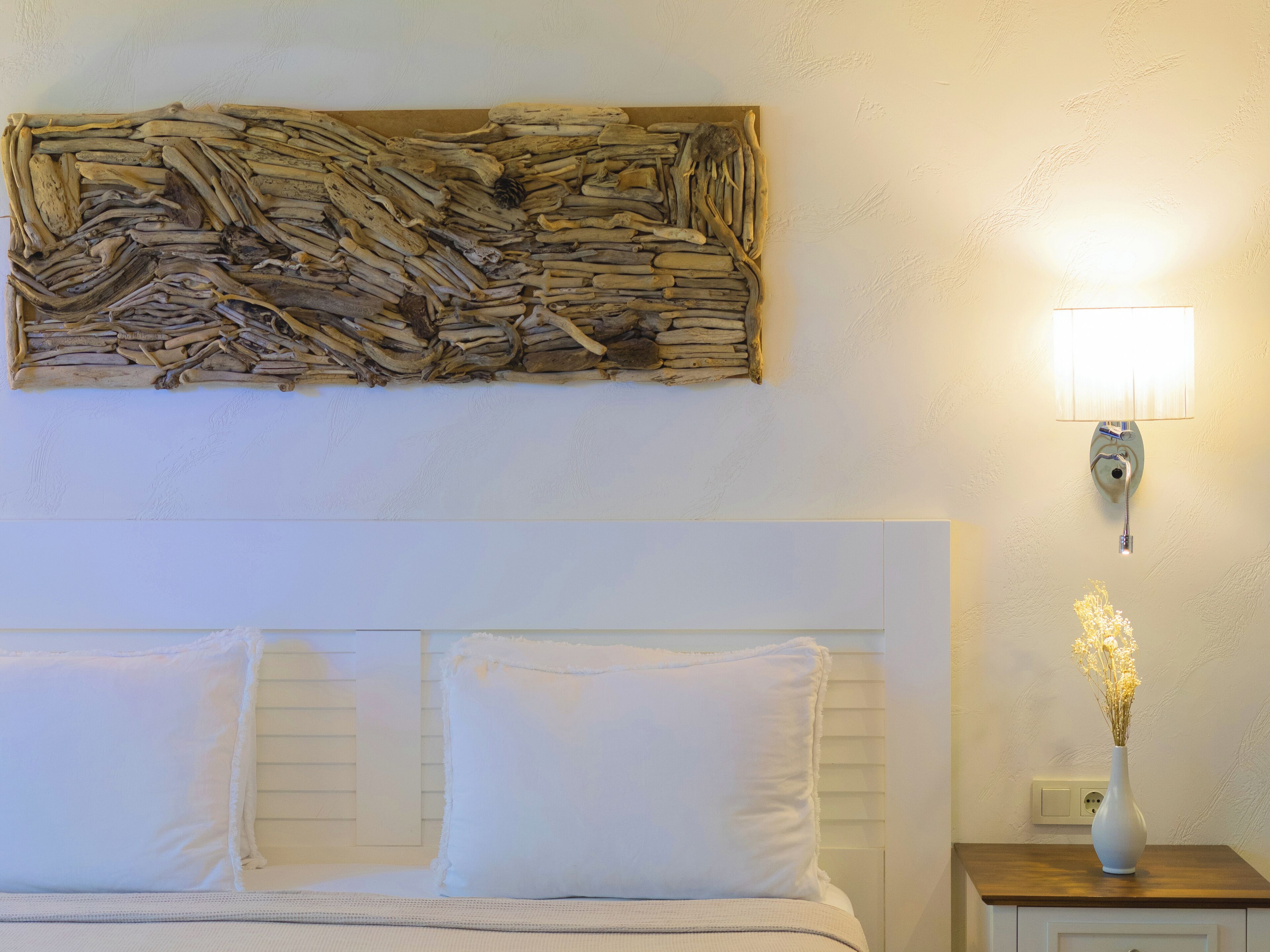 Un dormitorio con cama, almohadas, mesita de noche, lámpara de pared y un elemento decorativo en la pared.