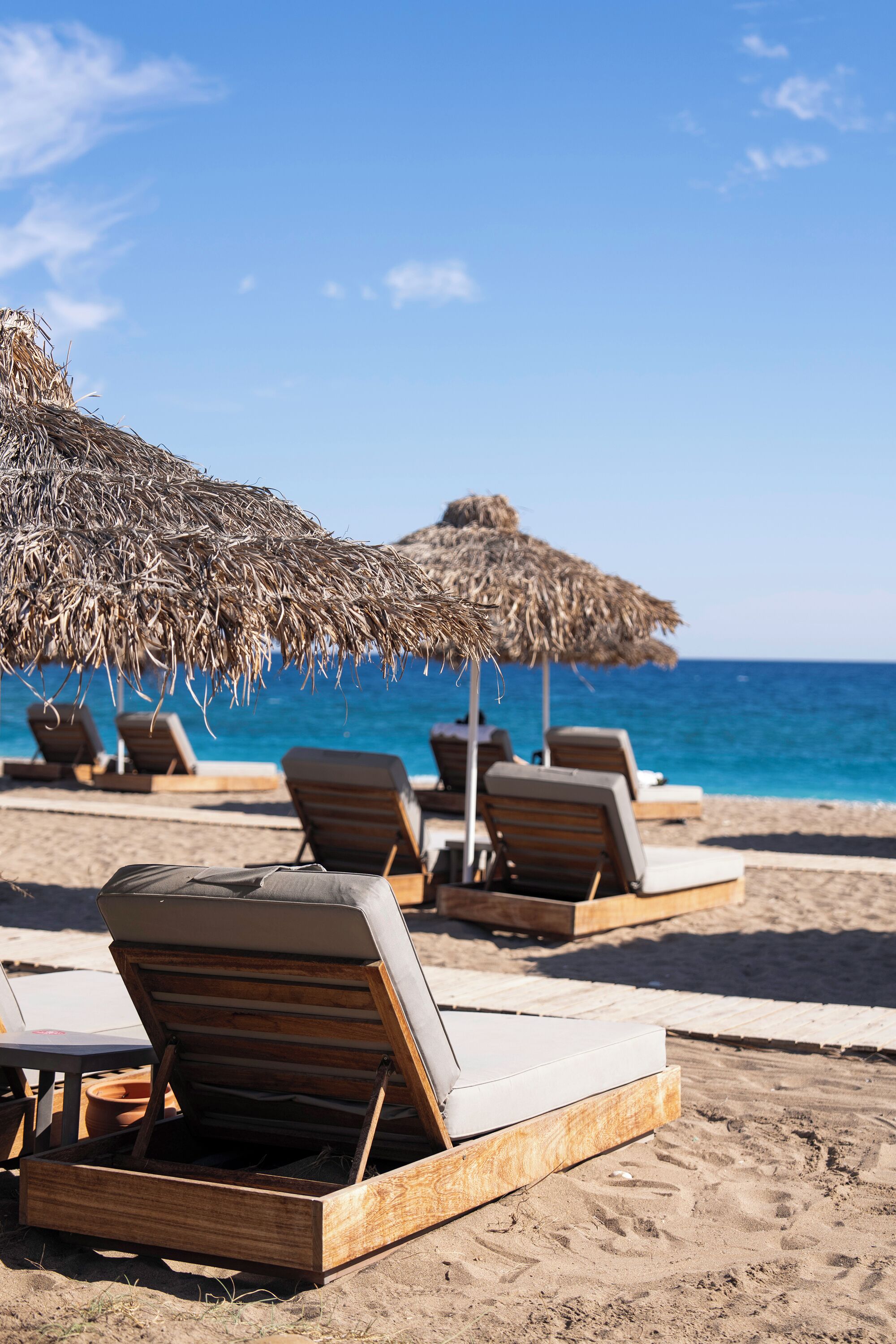 A beachside lounge area with wooden lounge chairs and thatched umbrellas.