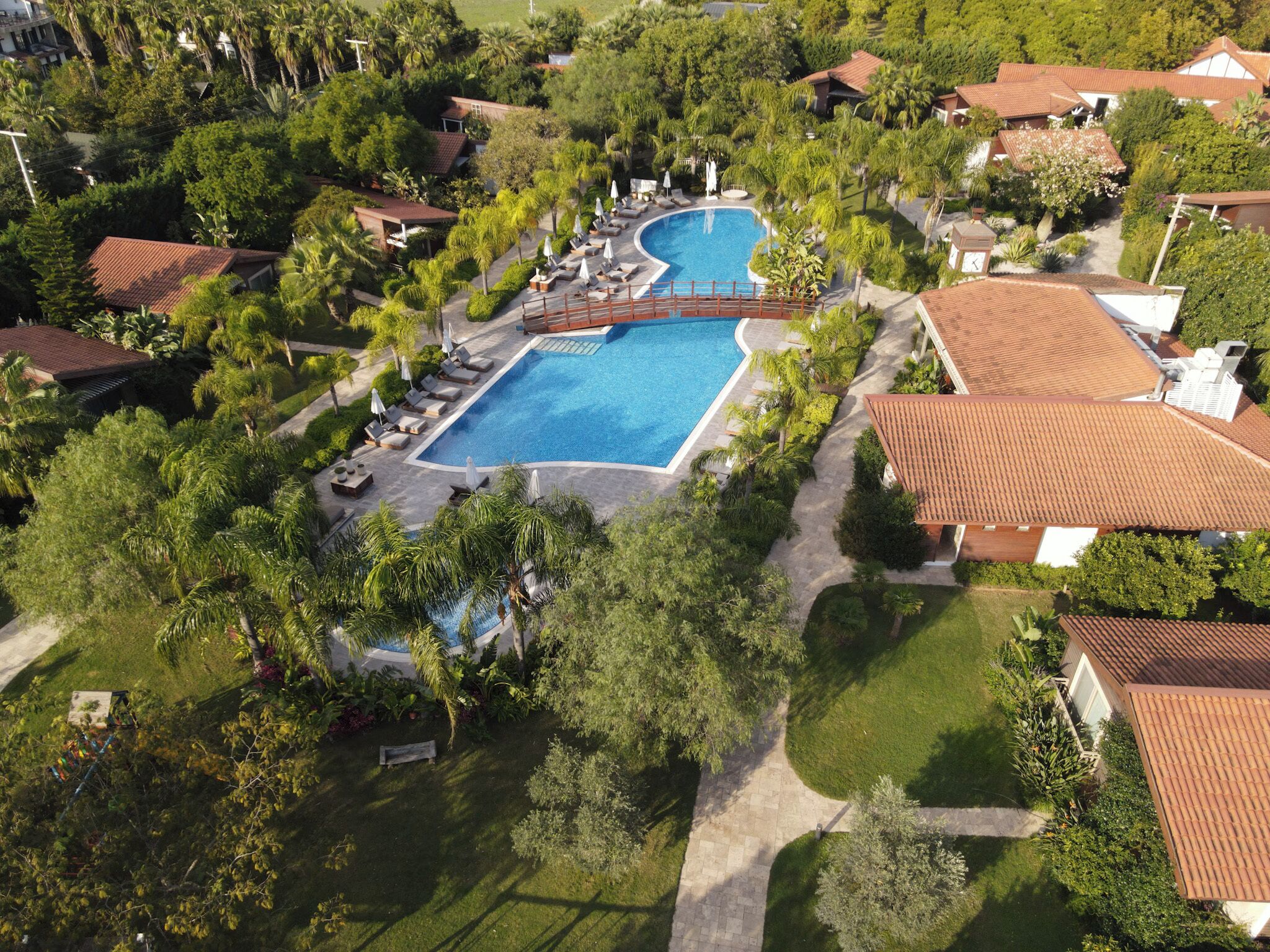 Eine Vogelperspektive zeigt ein Resort mit einem großen Schwimmbad, umgeben von üppiger Vegetation und Palmen.