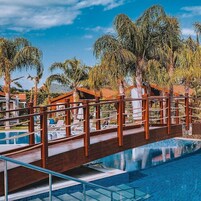Un área de piscina con barandillas de madera y sillas de descanso, rodeada de palmeras.