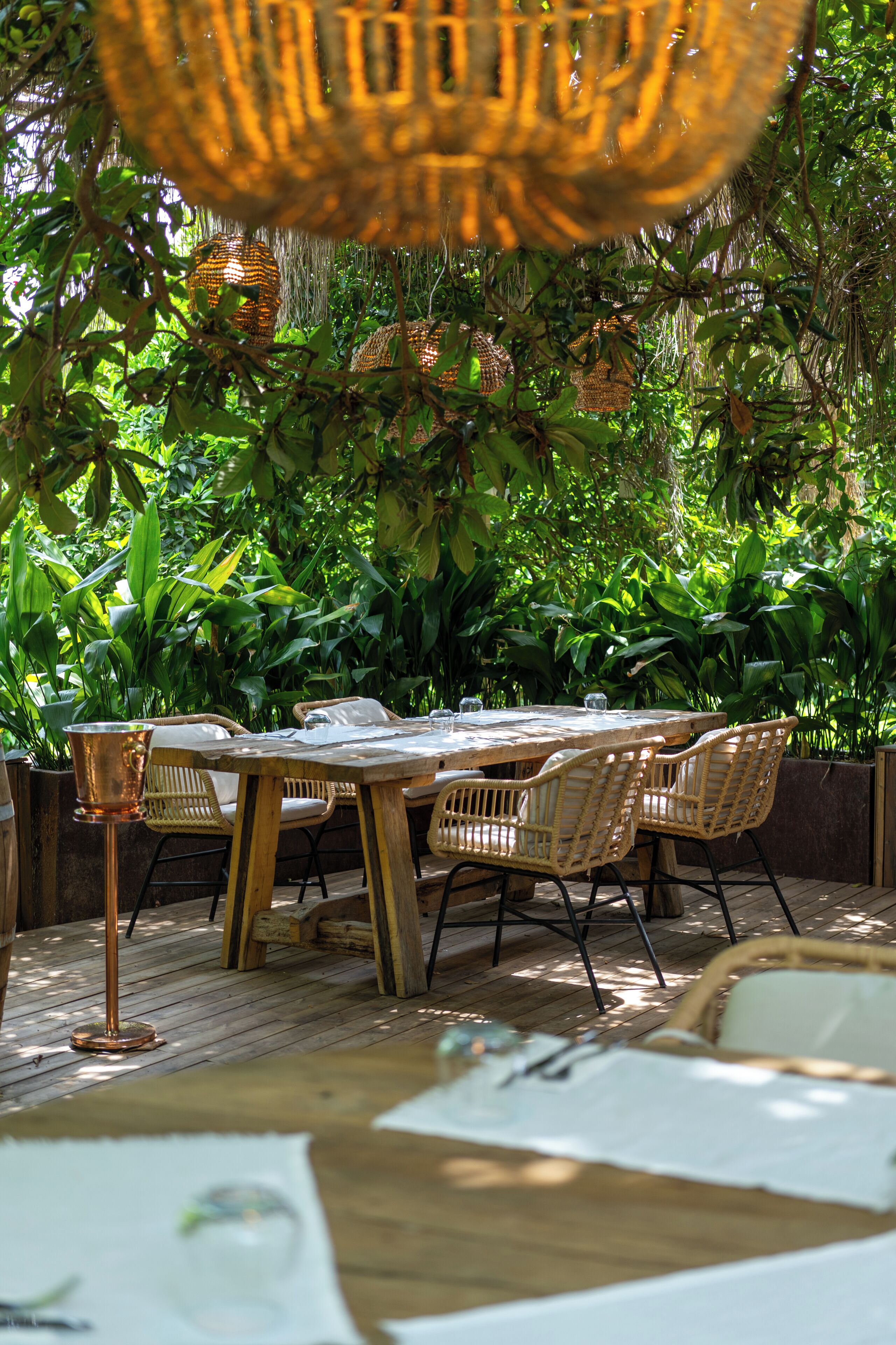 Un área de comedor al aire libre con mobiliario de mimbre y una base de mesa de cobre.