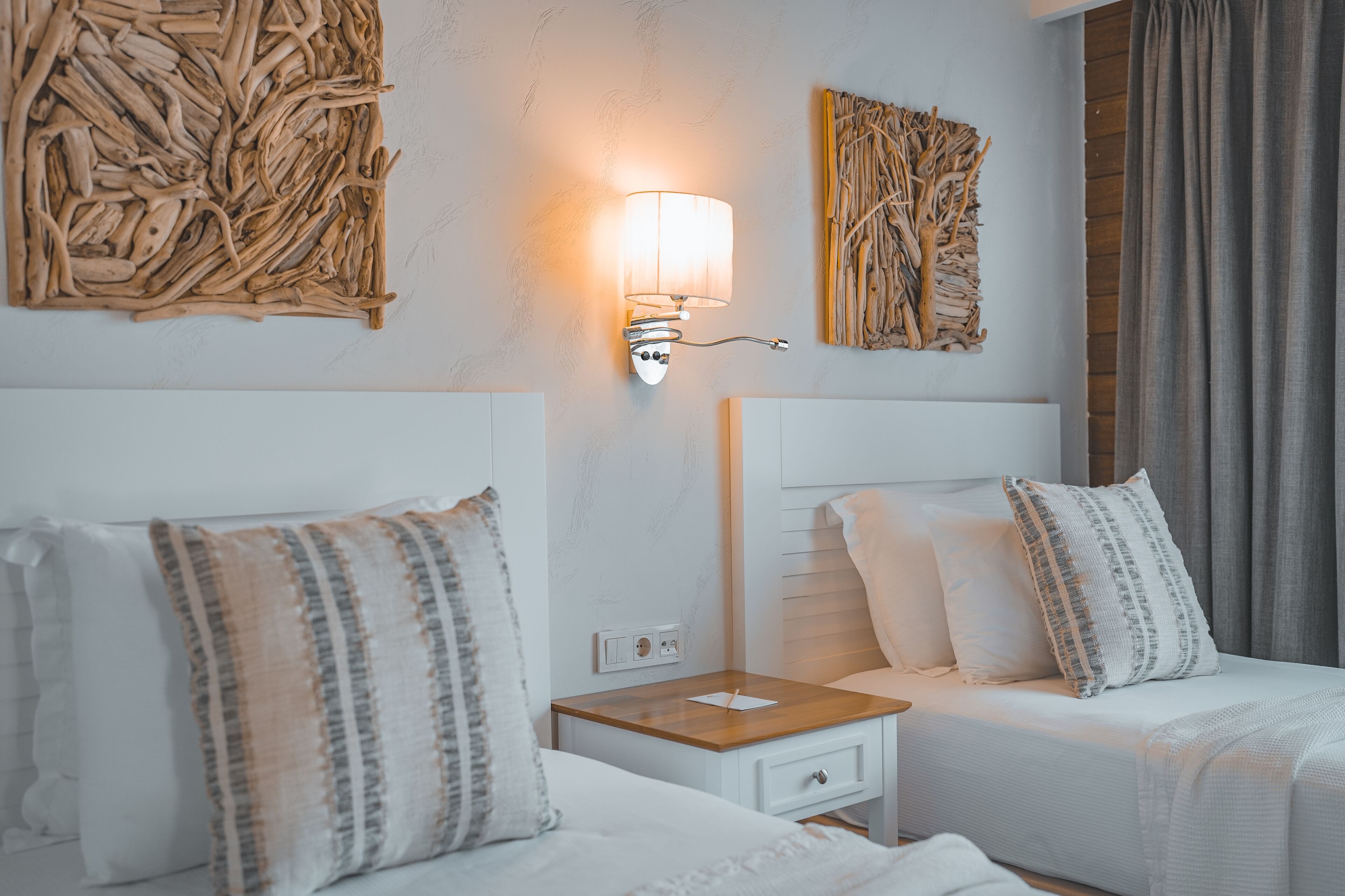 Habitación de hotel con dos camas, una mesita de noche, una lámpara de pared y dos obras de arte colgadas.