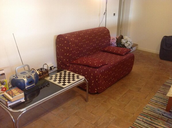 A living room with a red sofa, a glass coffee table with a chessboard, a kettle, and a small basket. - B&B Duomo (Orvieto)