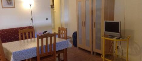 Un coin repas comprenant une table, des chaises, un téléviseur posé sur un meuble et un buffet avec des paniers.
