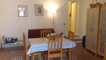 A dining area with a table set for four, surrounded by wooden chairs. There is a bench against the wall, a lamp on the table, and a cabinet with baskets on top.