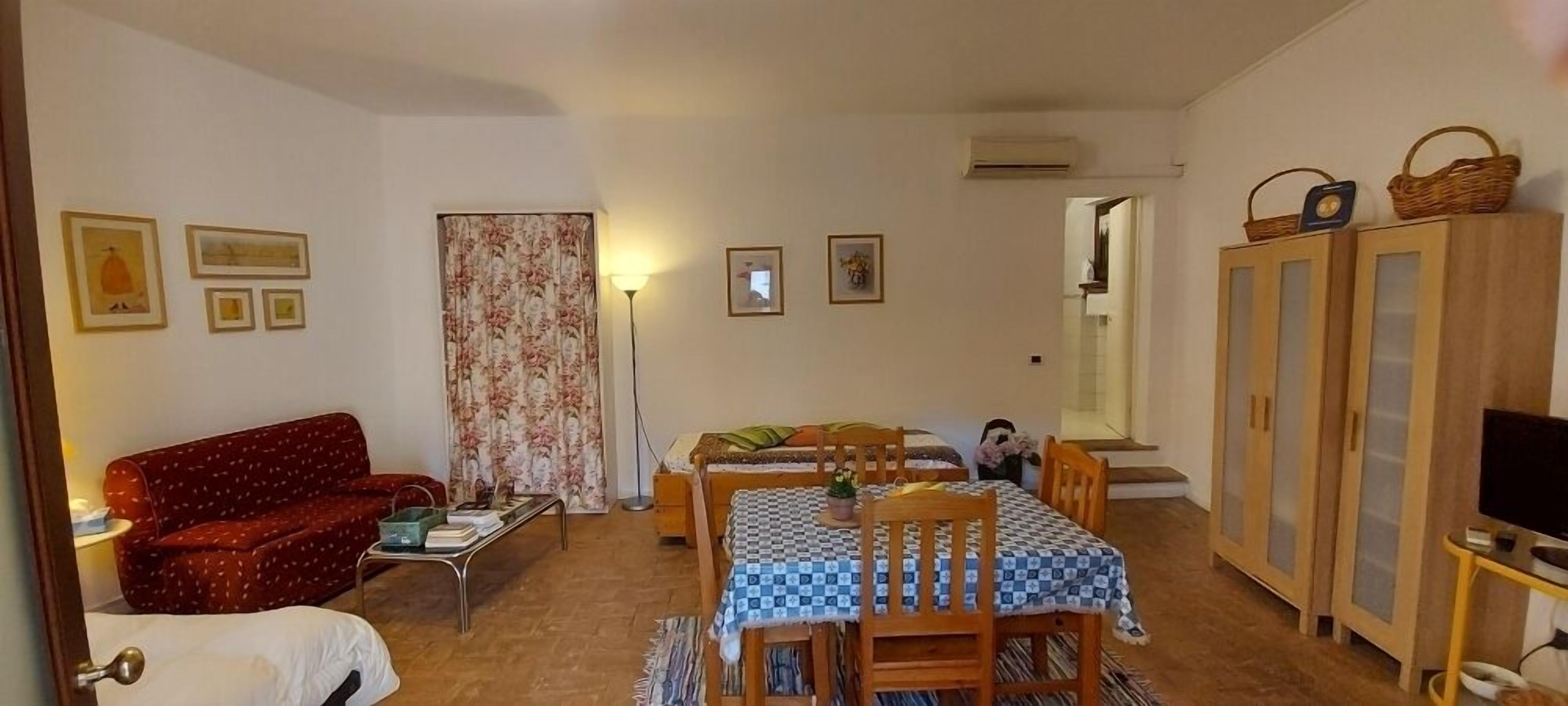 A cozy living room with a sofa, a dining table with chairs, a TV on a stand, and a cabinet with baskets.