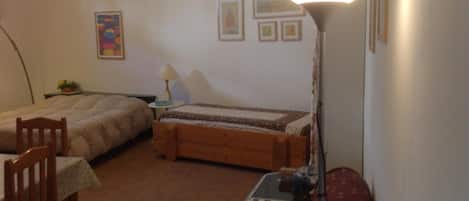 Una habitación pequeña y acogedora con dos camas individuales, un escritorio con computadora, una silla y una lámpara.