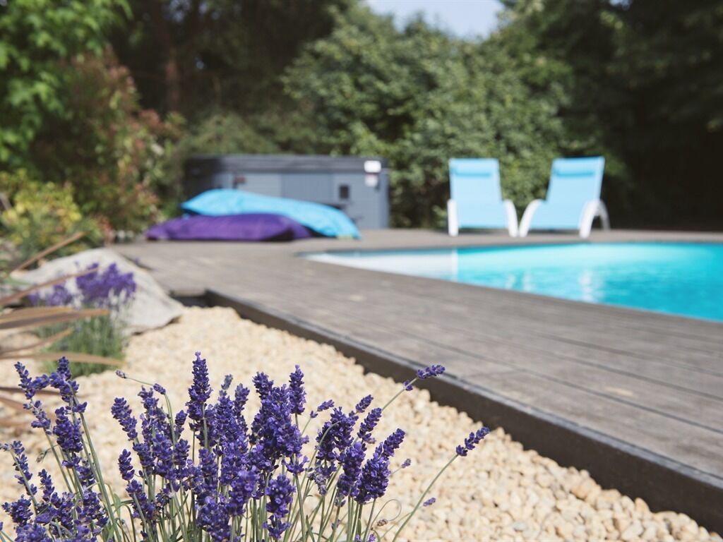 A wooden deck leading to a pool with two lounge chairs and a blue umbrella in the background.