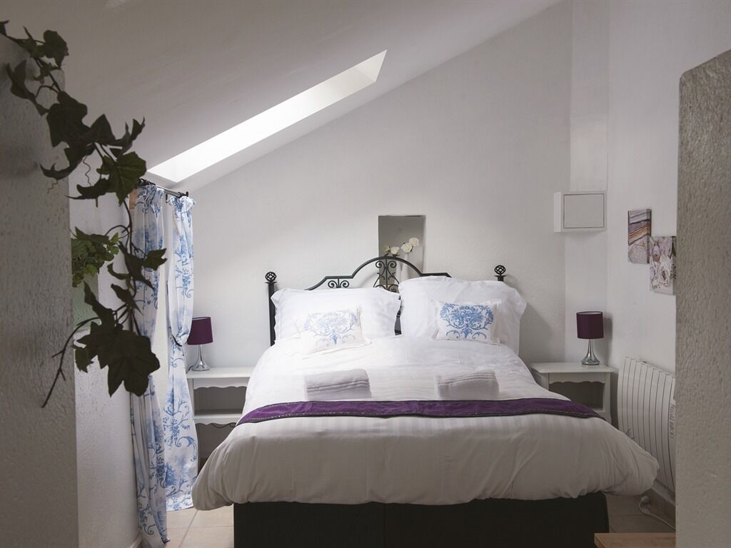 Een slaapkamer met een bed, nachtkastje, lamp en raam met uitzicht op de lucht.