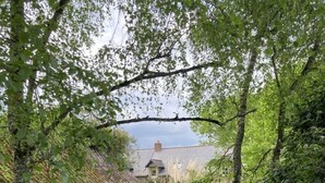 A lush garden with a stone wall, a grassy lawn, and a traditional house in the background. - La Marmoire (Soudan)