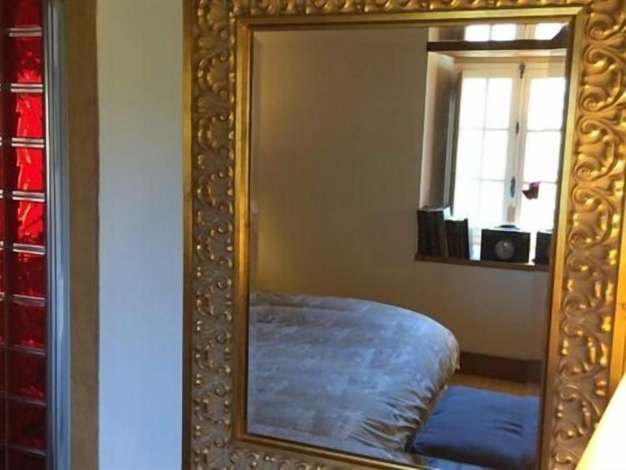 A bedroom with a large ornate mirror, a bed with a blue pillow, and a window with blinds.