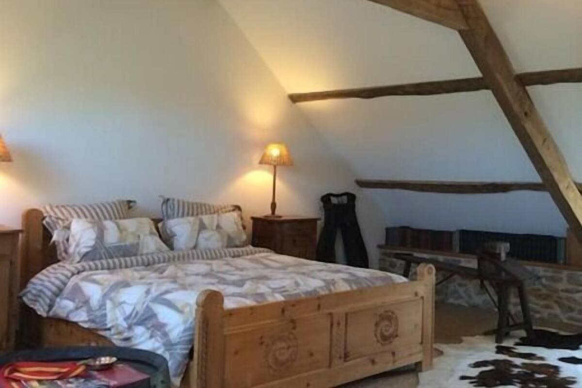Een gezellige slaapkamer onder de dakpannen met een houten bed, een lamp en een kleden van runderleer.