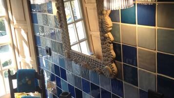 Un baño con un lavabo blanco, paredes con azulejos azules, un espejo decorativo y una ventana.