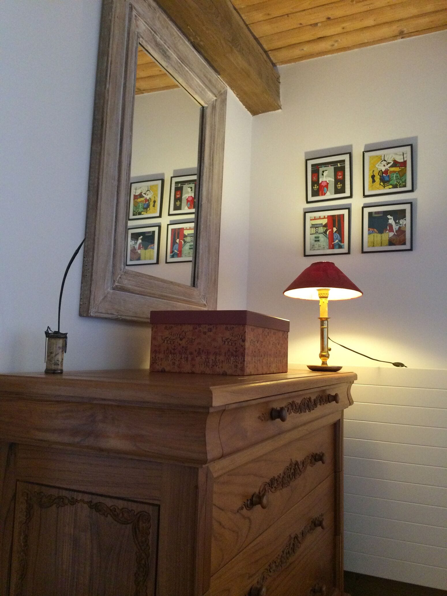 A wooden dresser with a mirror above it and a lamp on top. There are framed pictures on the wall behind the dresser.