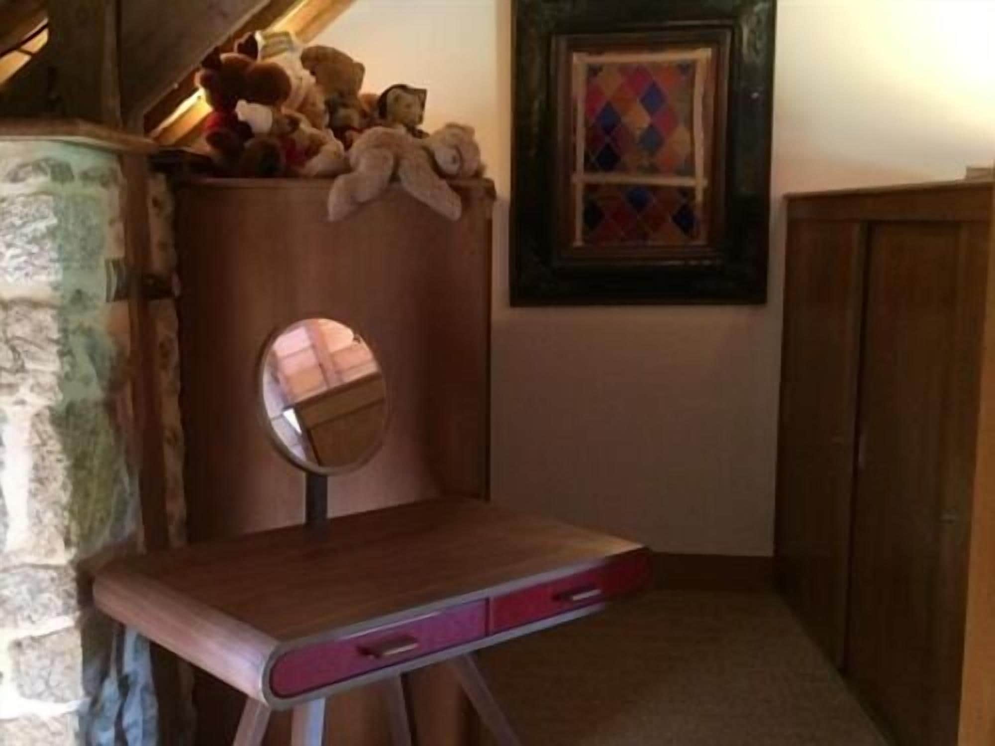 A wooden vanity with a mirror, a small drawer, and a shelf with stuffed animals.