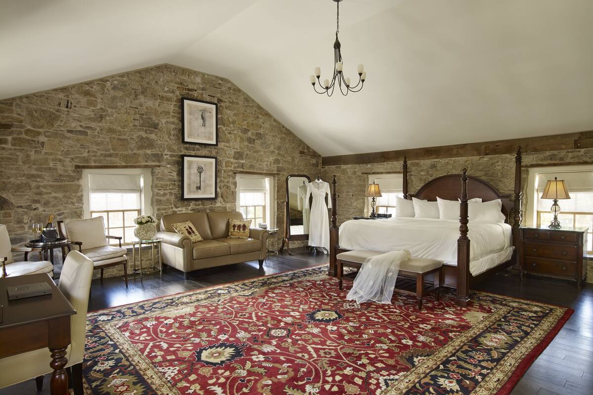 A spacious bedroom with a large bed, a stone wall, a chandelier, and a red patterned rug.