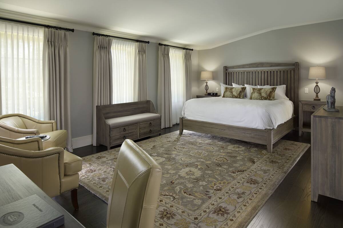 A hotel room with a large bed, a sofa, a desk, and a chair. There are curtains and a rug on the floor.