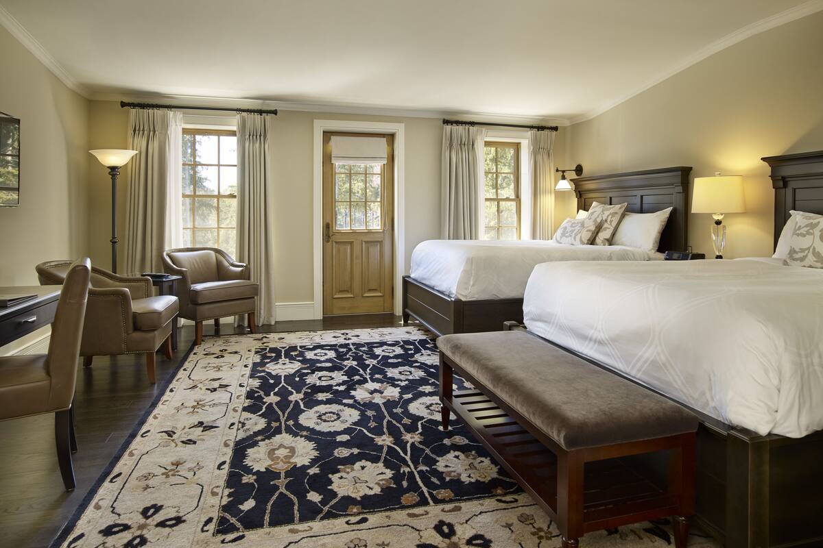 A hotel room with two beds, a desk, a chair, and a large patterned rug.