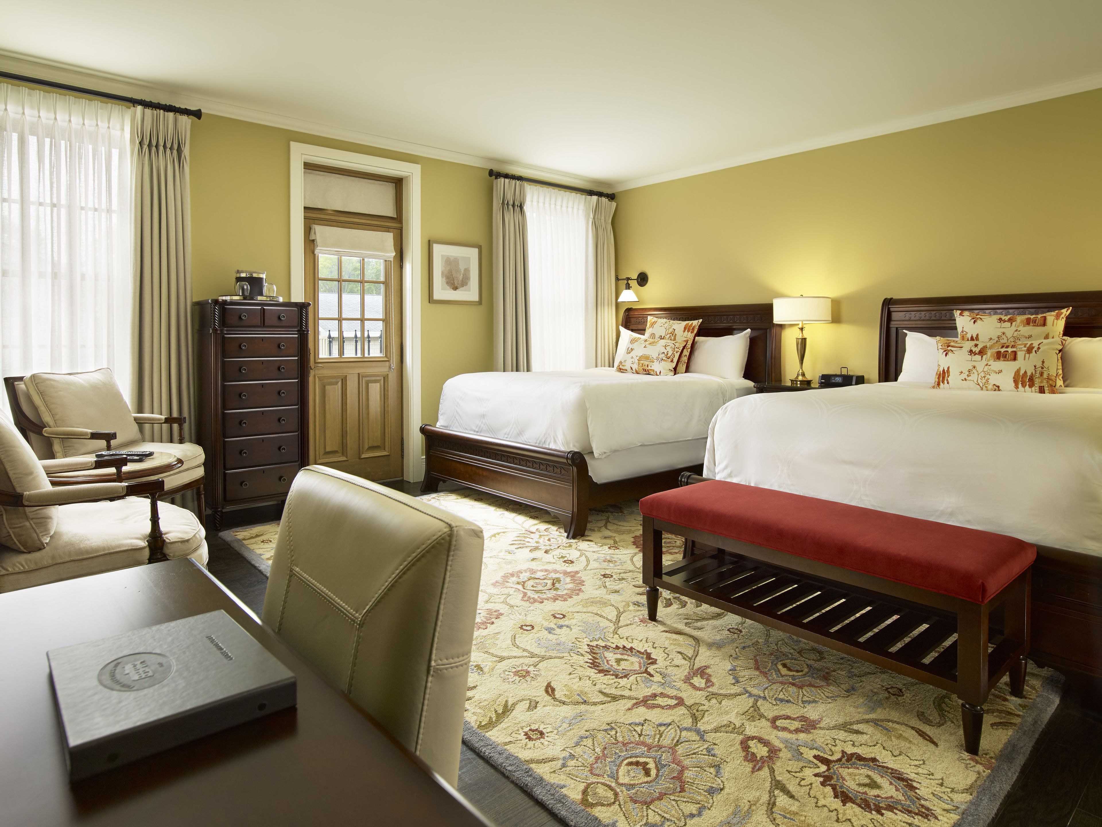 A hotel room with two beds, a desk, a chair, a dresser, and a carpeted floor.