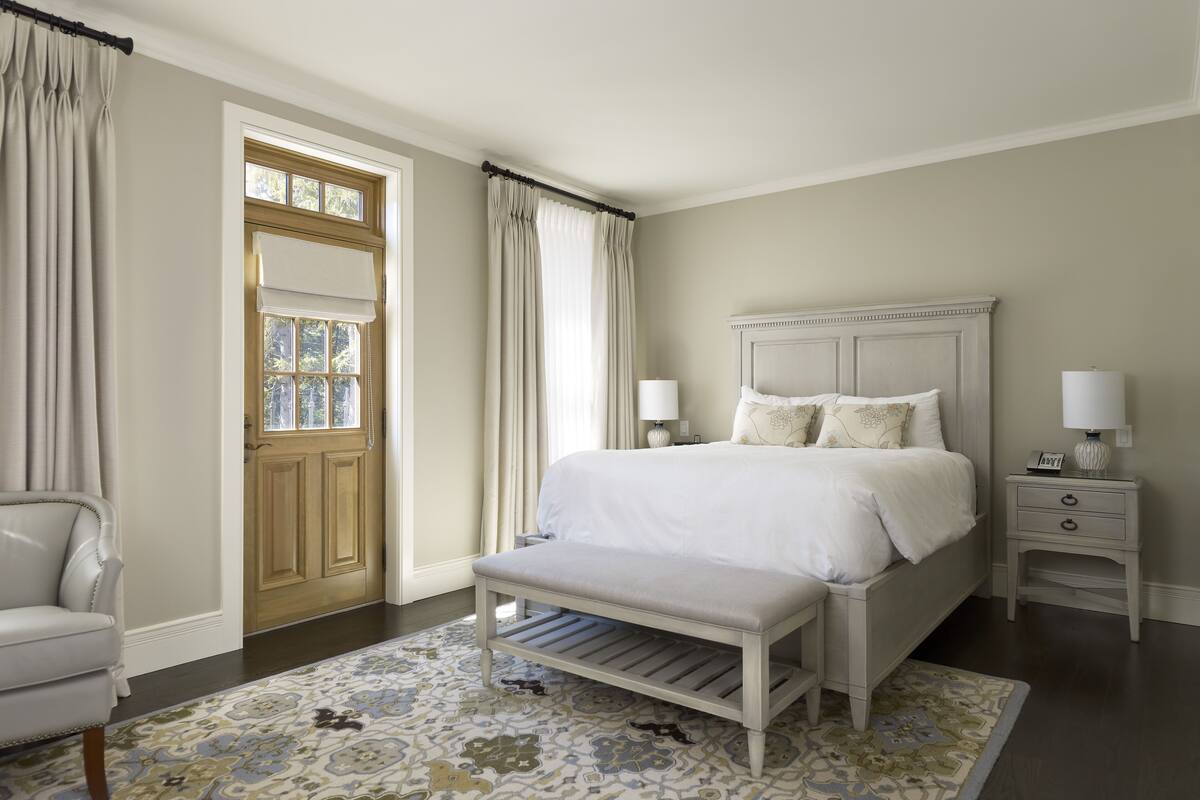 A neatly arranged bedroom with a bed, bedside tables, a chair, and a patterned rug.