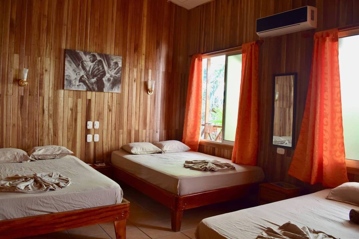 Quarto com duas camas, paredes de madeira, um quadro e um aparelho de ar condicionado.