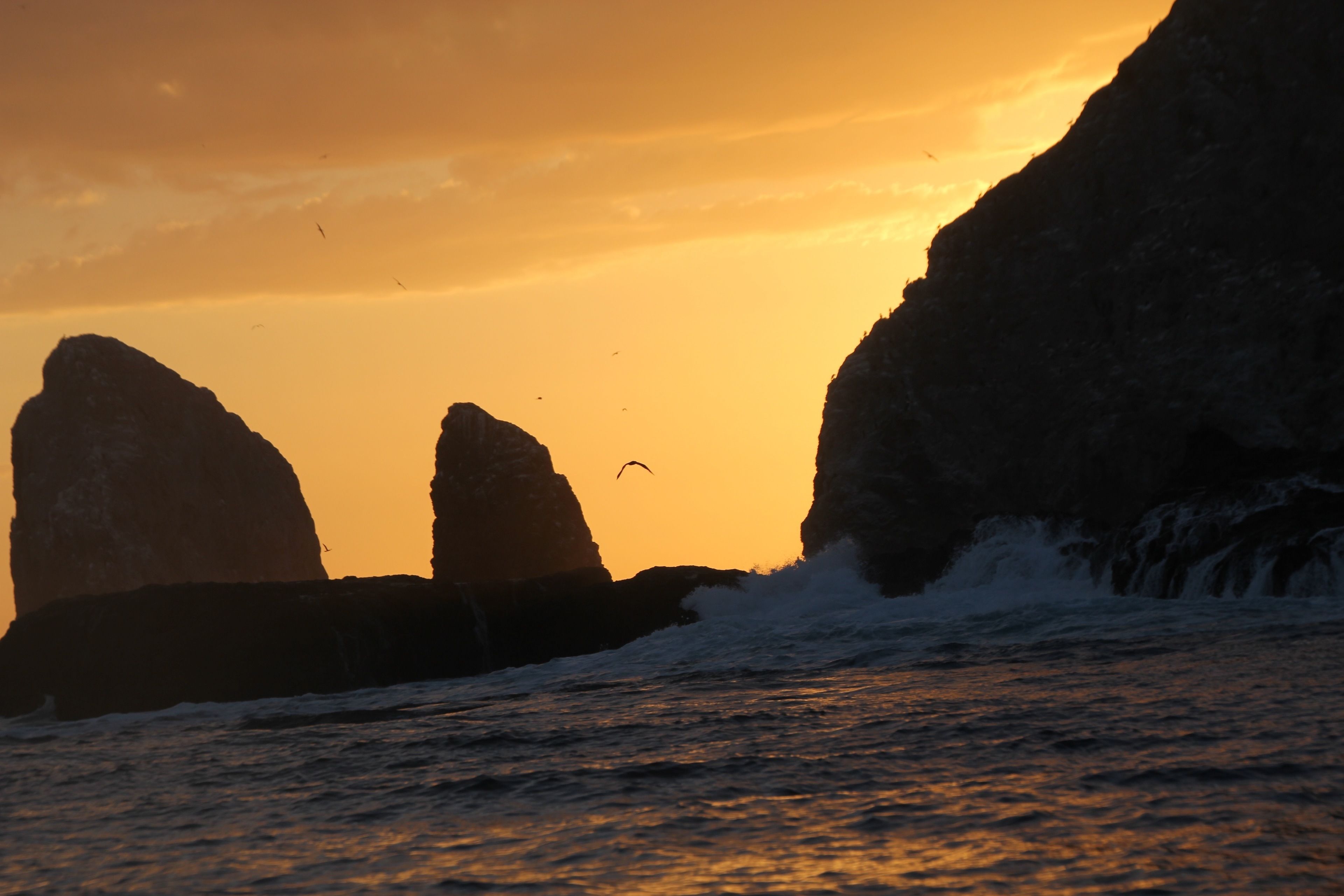 A coastal sunset with large rock formations silhouetted against the sky.