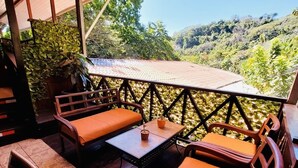 Un patio al aire libre con muebles de madera, una mesa y vistas a un paisaje verde y exuberante.