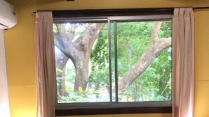 Una cama con una toalla dispuesta en forma de corazón, una ventana con cortinas y una lámpara de noche.