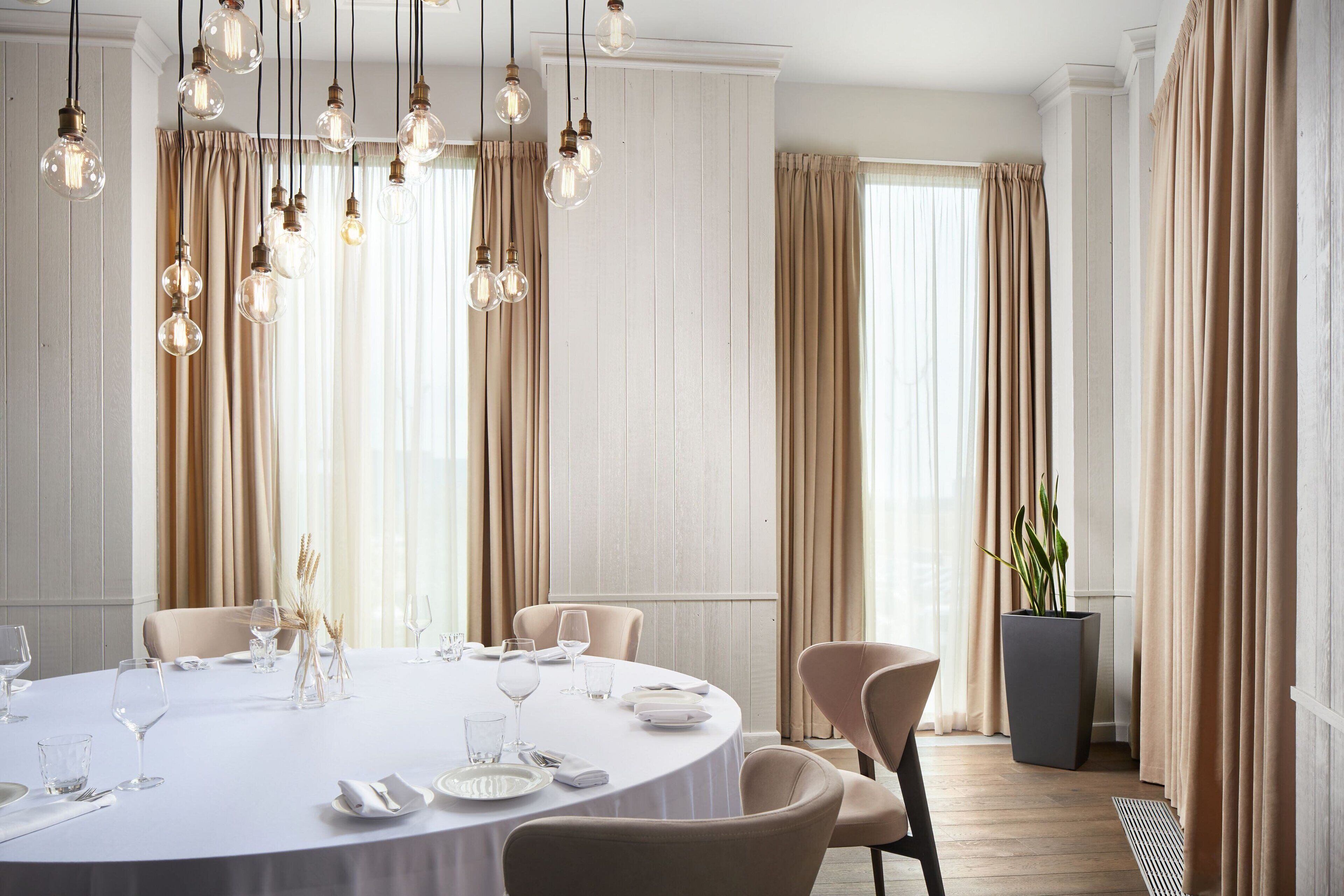 Un coin repas avec une table ronde dressée pour un repas, entourée de chaises, et un luminaire suspendu au-dessus.