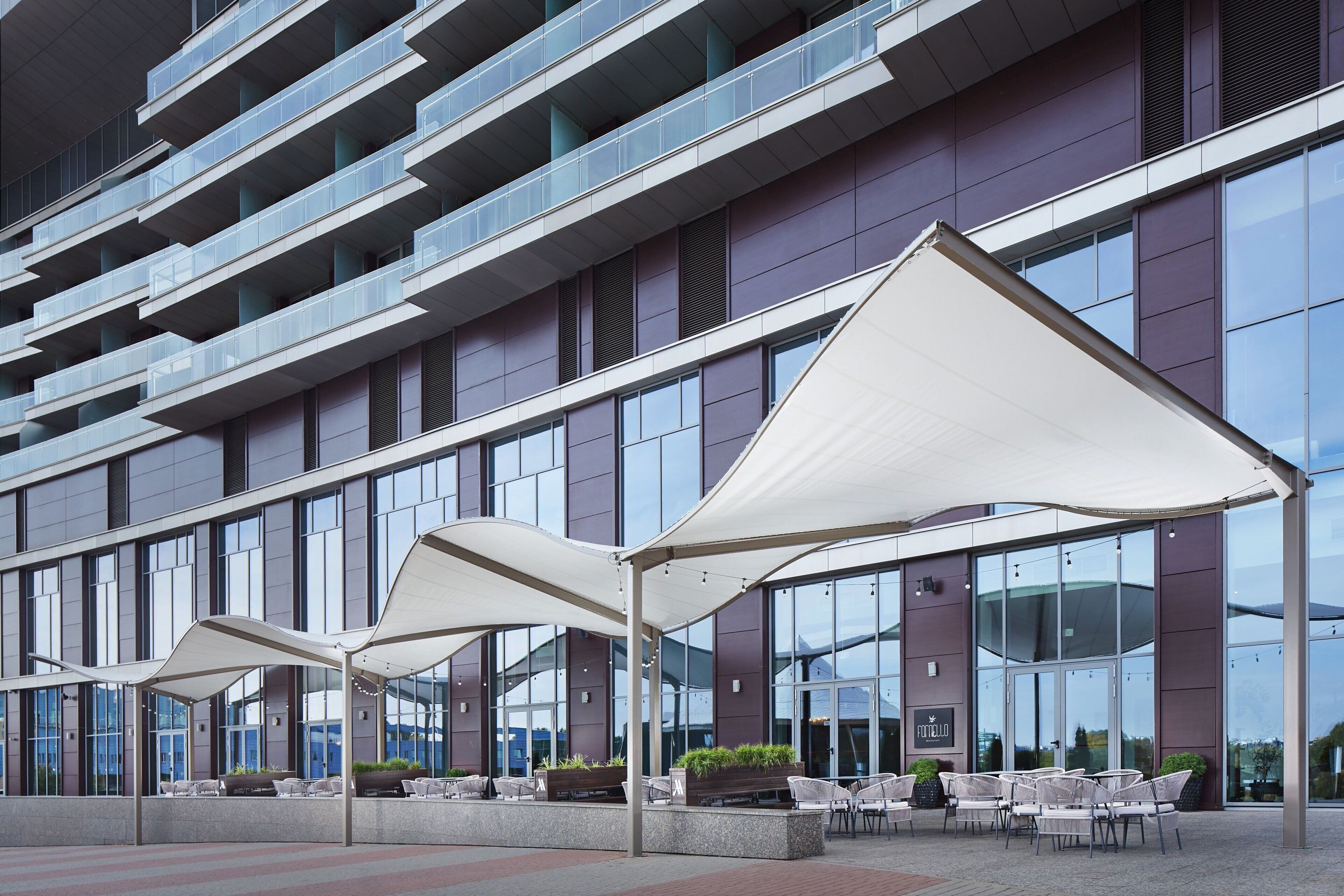 A modern hotel exterior with outdoor seating and a glass facade.