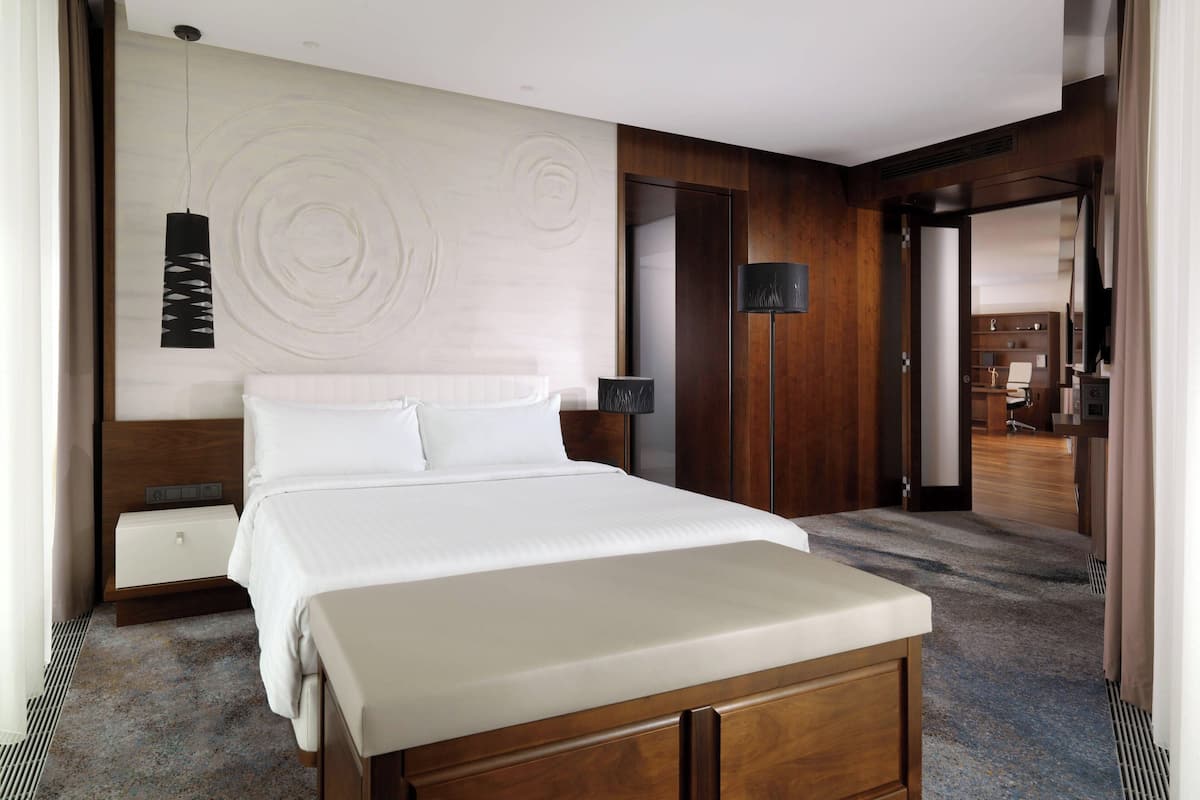 Une chambre d’hôtel avec un grand lit, une tête de lit en bois, une table de chevet, une lampe et une vue sur l’intérieur de l’hôtel.