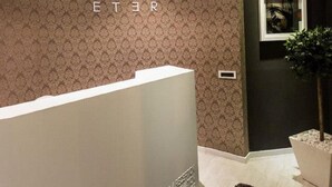 Un espace d’accueil au design moderne, comprenant un mur décoré d’un motif, un comptoir de réception et une plante en pot.