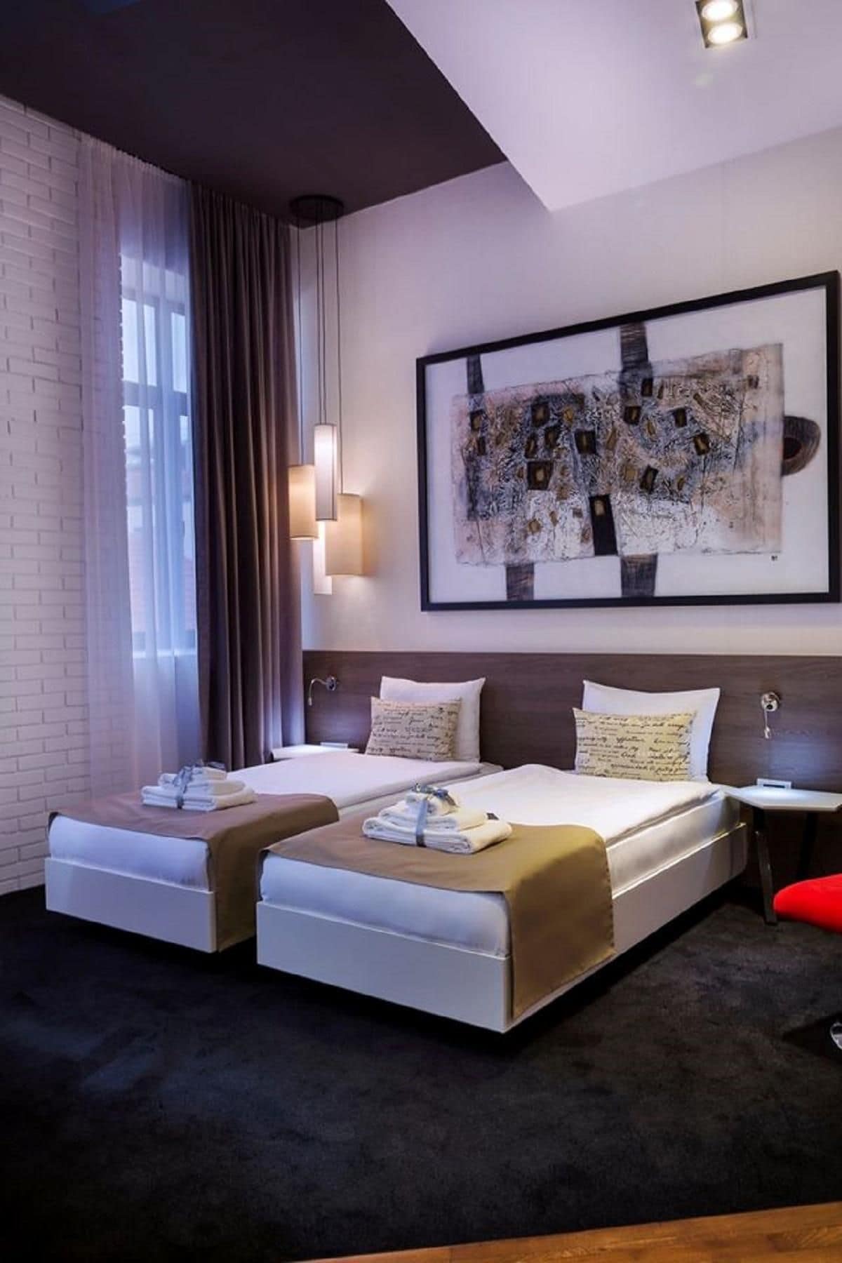 A modern hotel room with a large bed, a bedside table, a wall-mounted artwork, and a window with curtains.