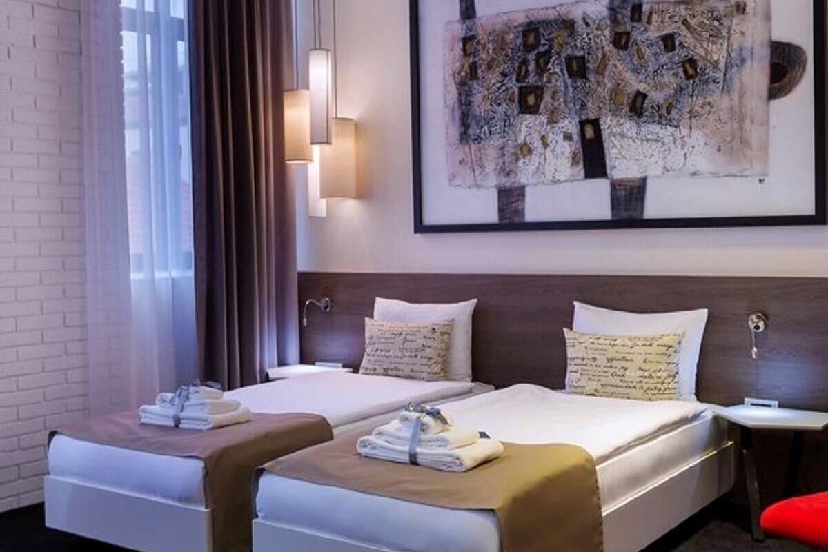 A modern hotel room with a large bed, a bedside table, a wall-mounted artwork, and a window with curtains.