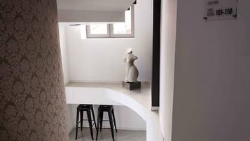 A modern interior with a white wall, a window, and a sculpture. There are two black stools under a white counter.