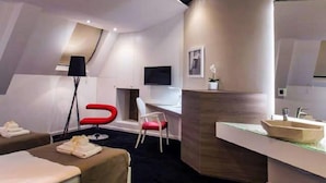 Une chambre d’hôtel moderne équipée d’un lit, d’un bureau, d’une chaise, d’une lampe de bureau, d’un miroir et d’une petite plante.