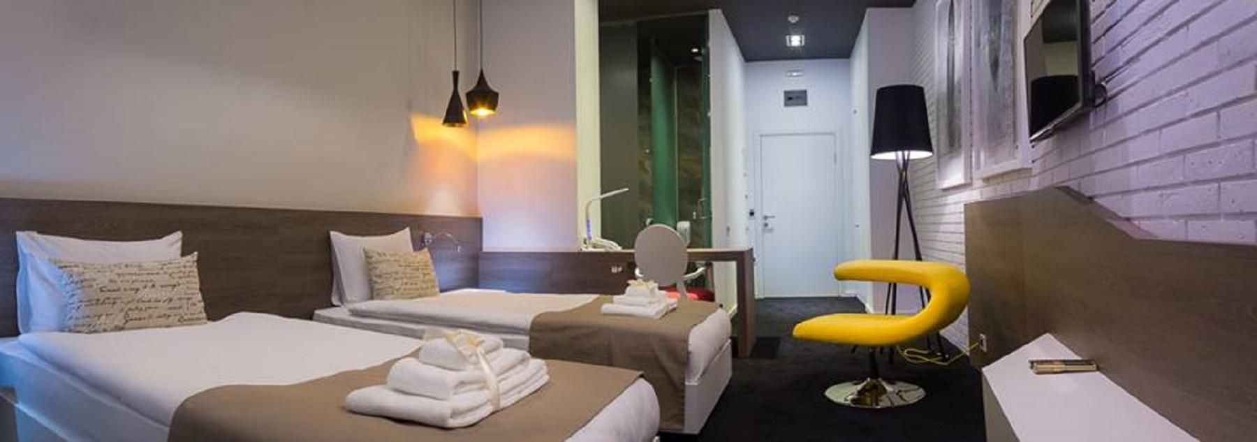 A hotel room with two beds, a mirror, a yellow chair, and a small table.