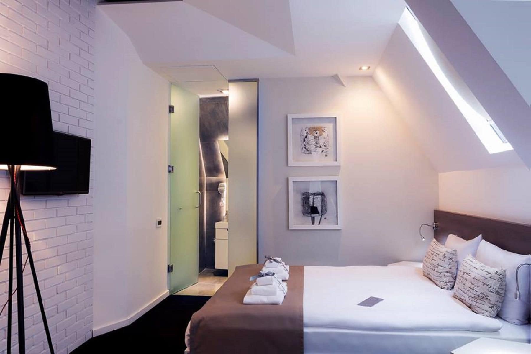 Ett modernt hotellrum med en säng, en platt-TV, konst på väggen och ett takfönster.