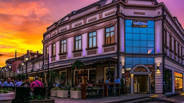 A building with a corner entrance, large windows, and outdoor seating. - Eter Hotel (Niš)