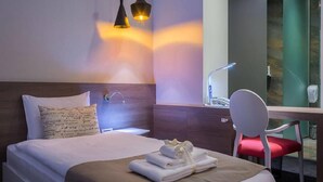 A hotel room with a bed, a desk with a chair, a nightstand, and a wall-mounted lamp. - Eter Hotel (Niš)