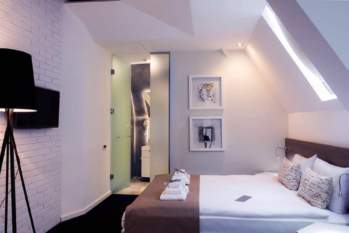 A modern hotel room with a bed, a flat-screen TV mounted on the wall, and artwork above the bed.