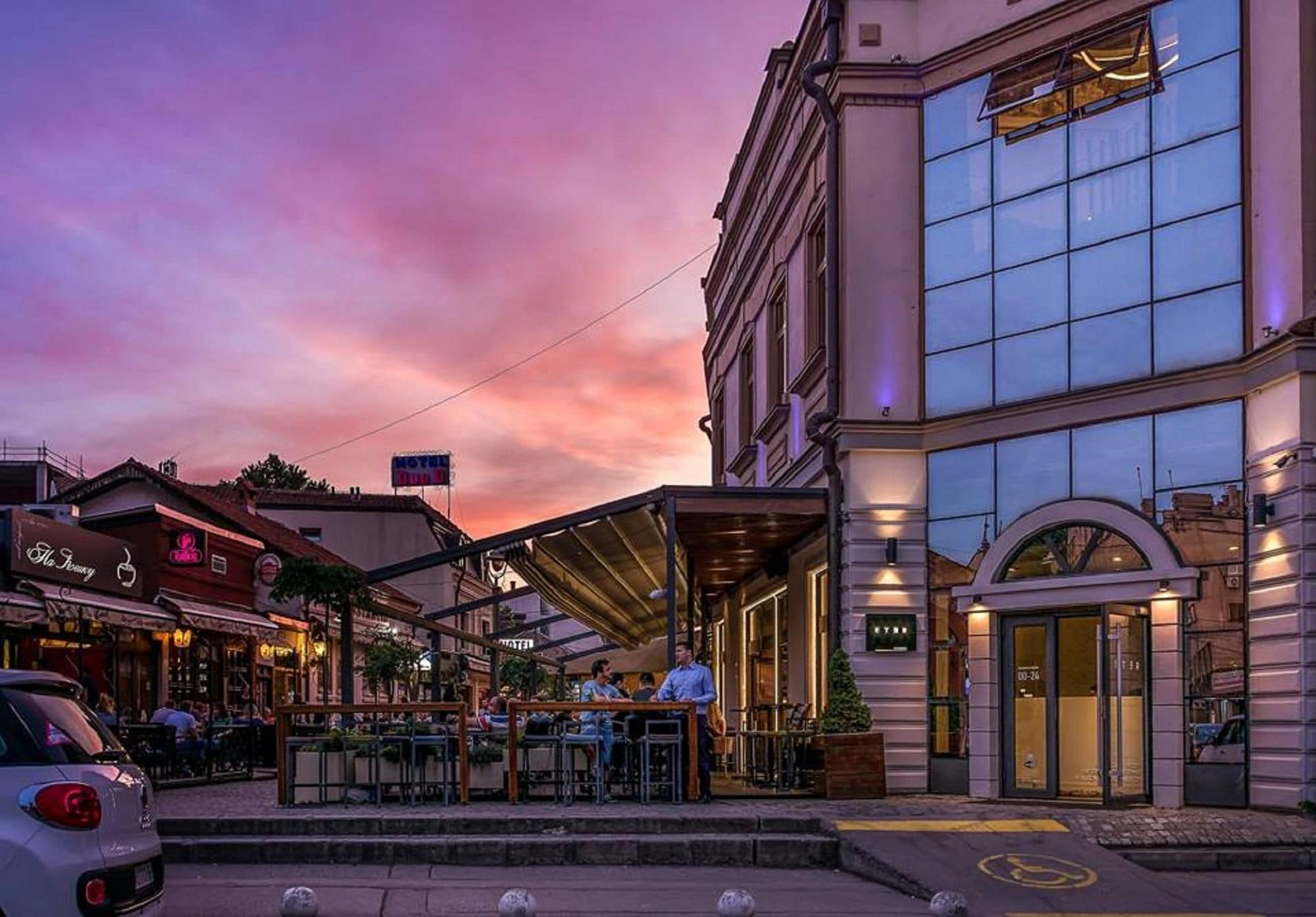 A hotel with a covered outdoor seating area and a modern building with large windows.