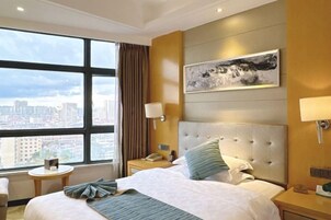 Habitación de hotel con un ventanal grande, una cama con cabecero, una mesita de noche y una obra de arte colgada en la pared.
