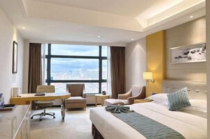 Habitación de hotel con cama, escritorio, silla y un amplio ventanal con vista a la ciudad.