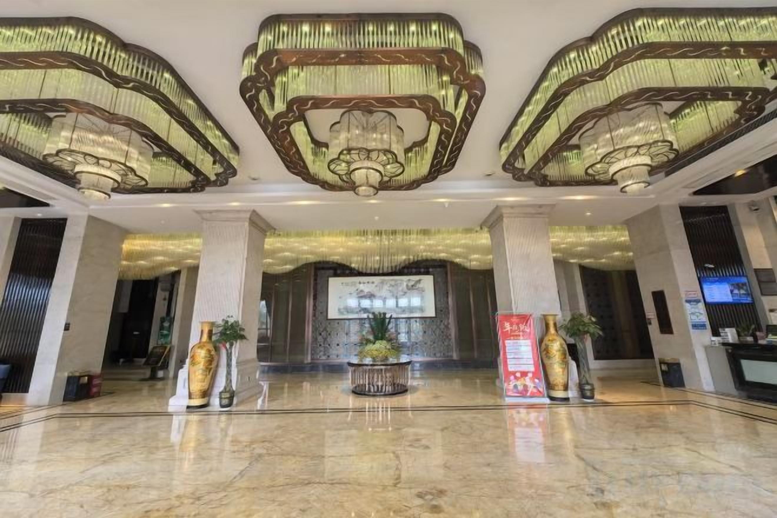 A hotel lobby with a marble floor, large chandeliers, and a reception desk.