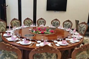 A round dining table with chairs, a floral centerpiece, and a flat-screen TV mounted on the wall.