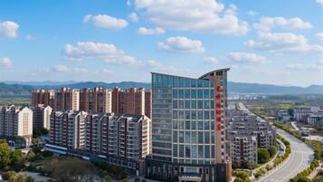 A high-rise residential building with multiple floors, surrounded by greenery and a clear sky.