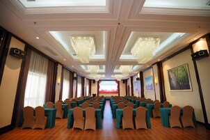 Un salón de conferencias con filas de sillas, un escenario al frente y candelabros.