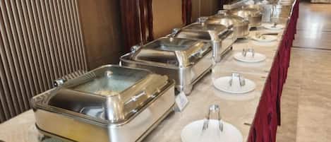 A buffet setup with multiple serving stations, each with a covered food container and a white plate.